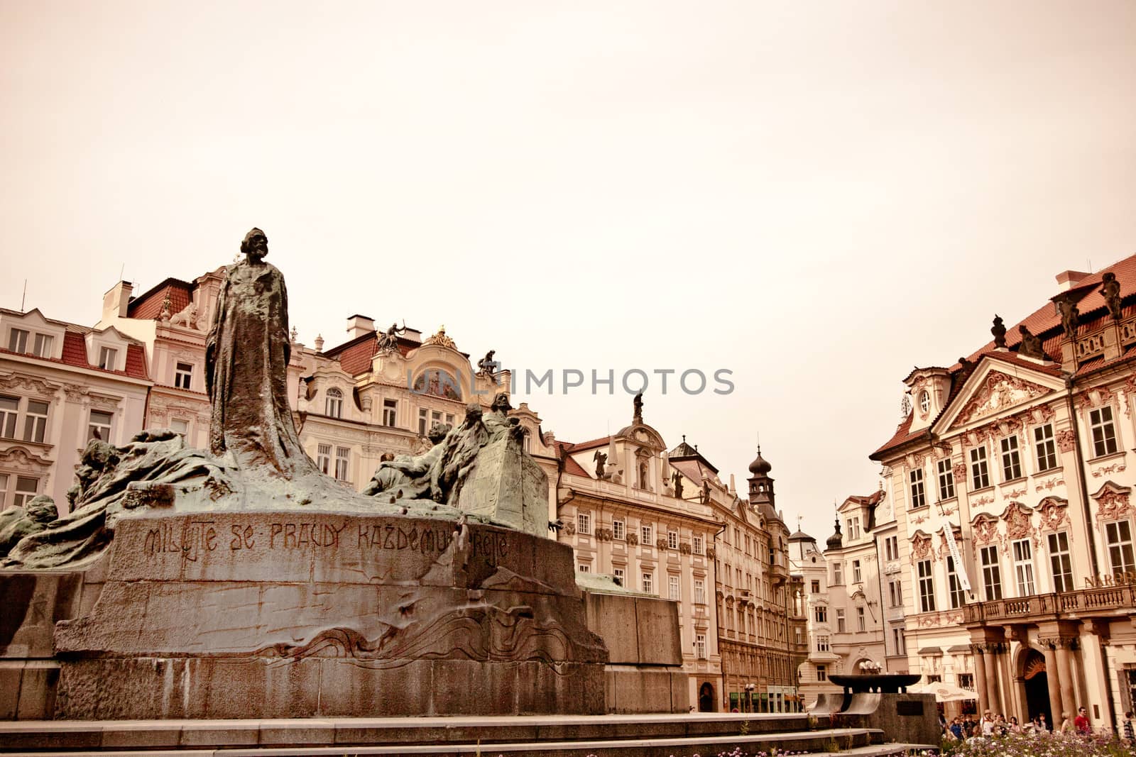 Aged image of central Prague with a low angle view of a figural fountain surrounded by historical buildings and architecture with a pink tone