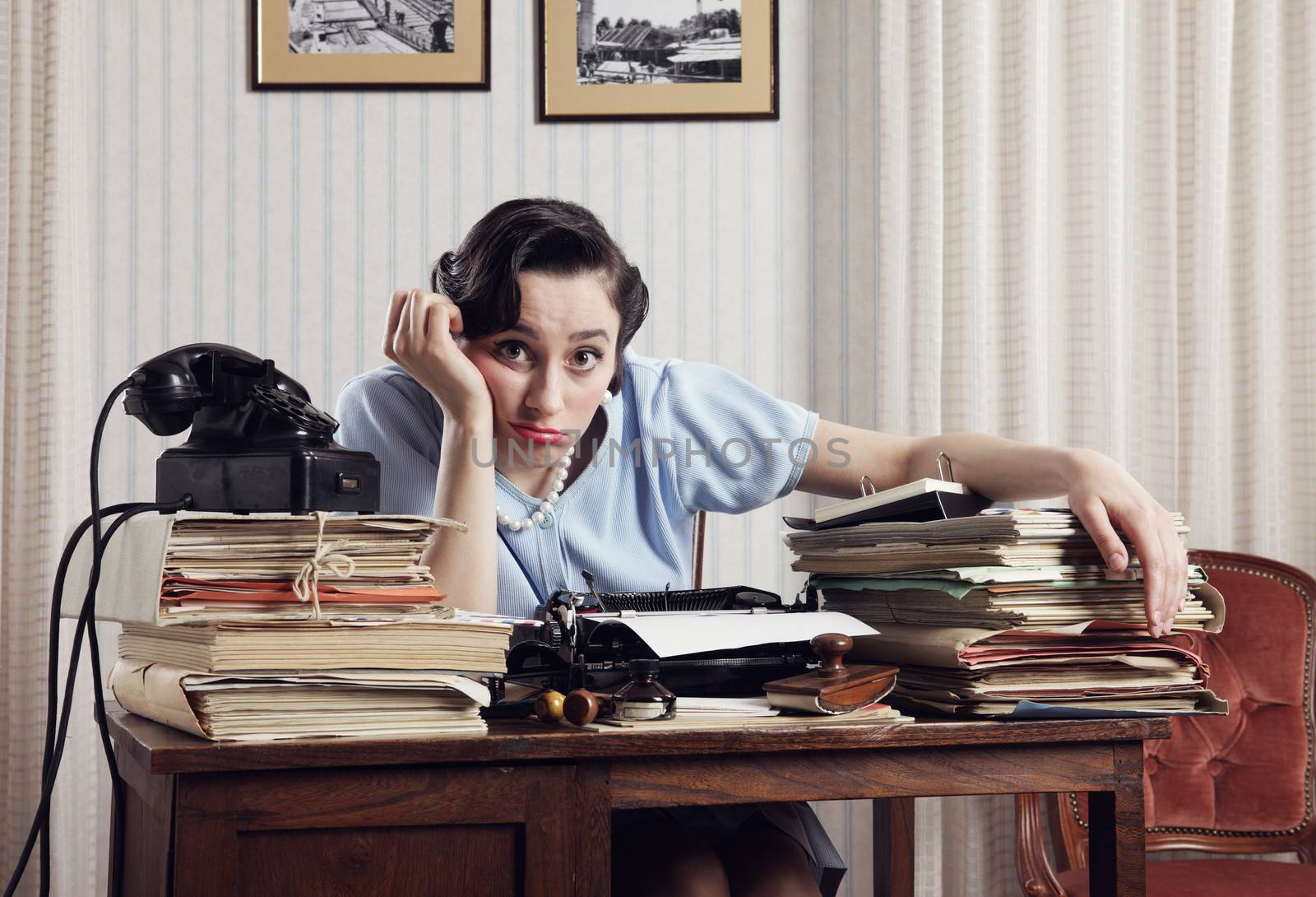 A bored office worker sitting behind a large stack of paperwork