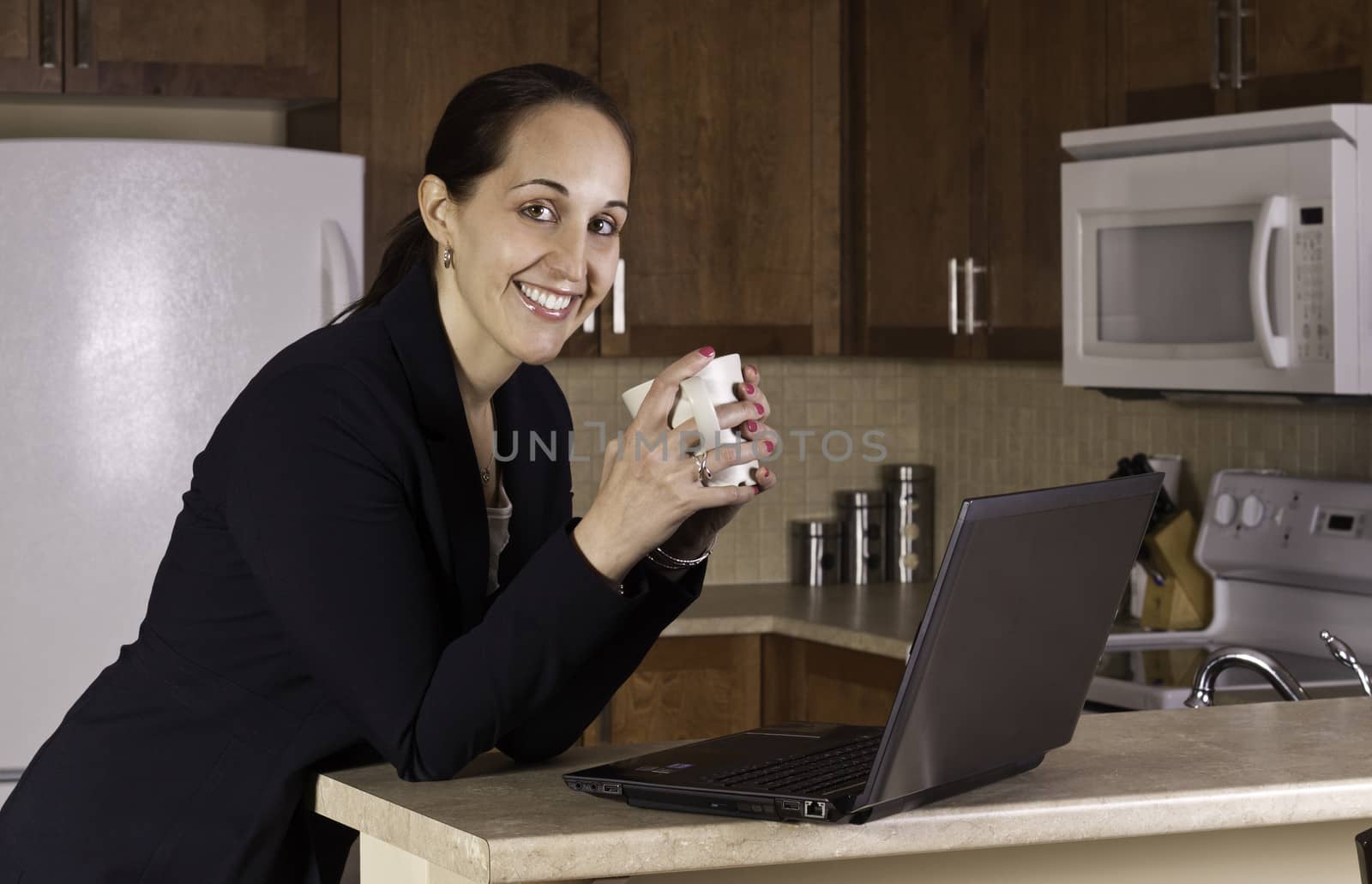 Business woman working on a laptop computer and drinking coffer in her kitchen.
