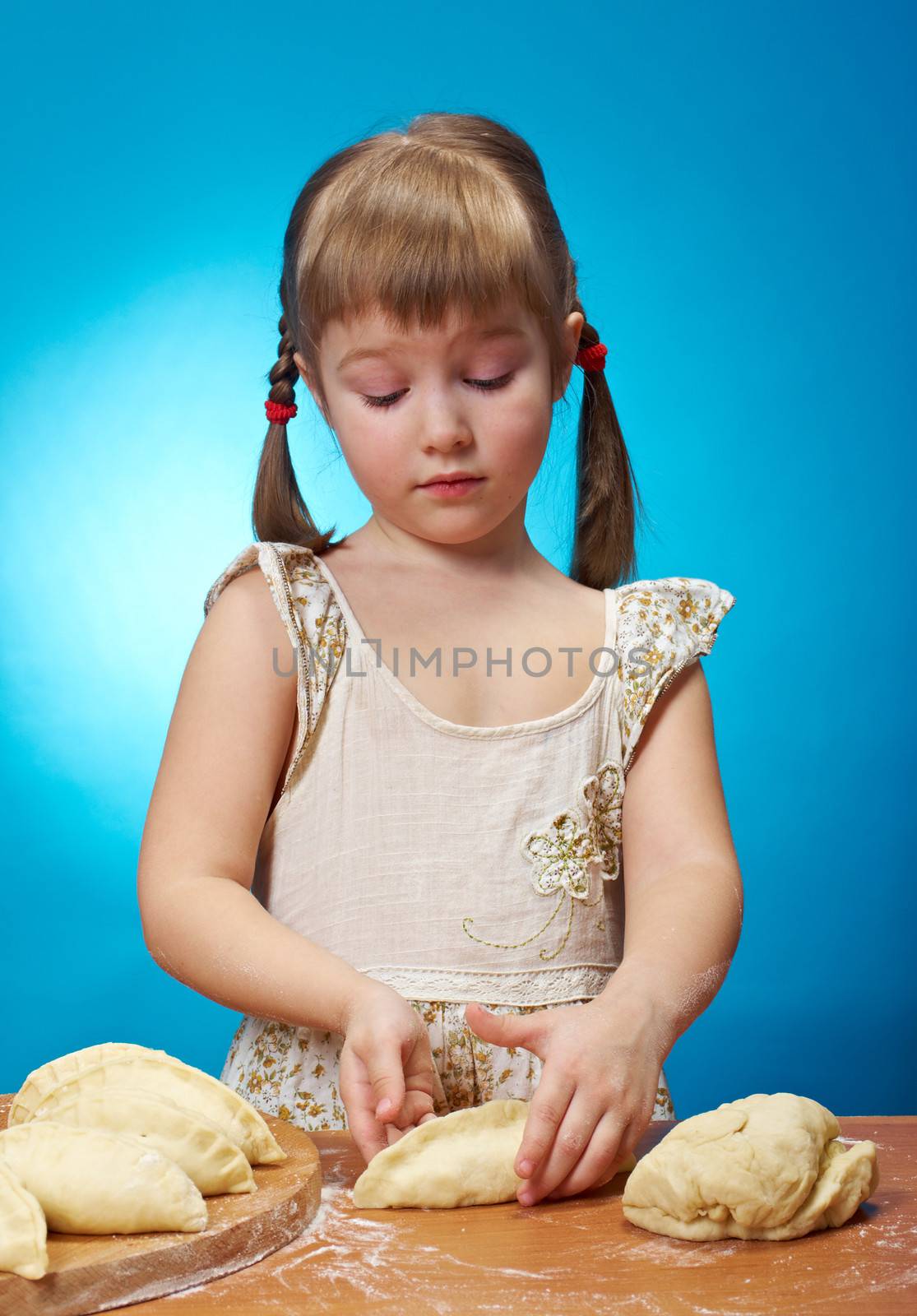 Smiling little girl kneading dough at kitchen with baking a pie