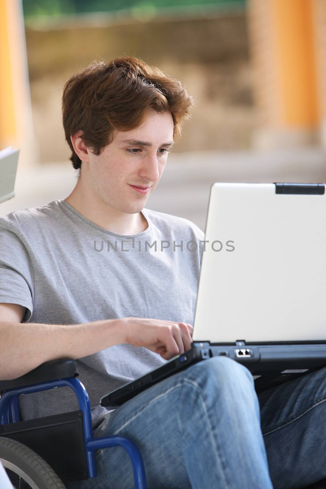 Disabled young man sitting in wheelchair using laptop