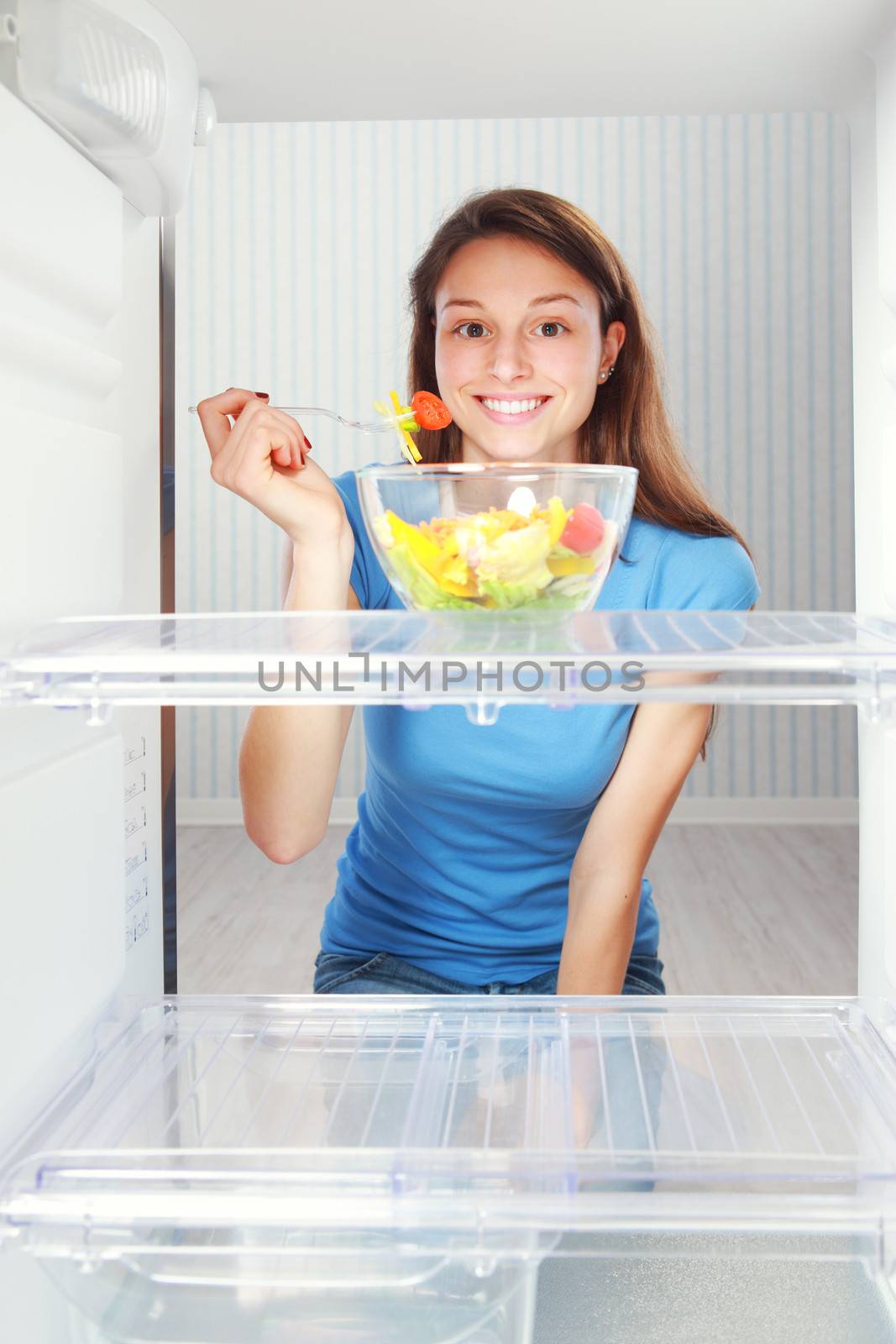 Beautiful healthy girl taking a salad from the refrigerator
