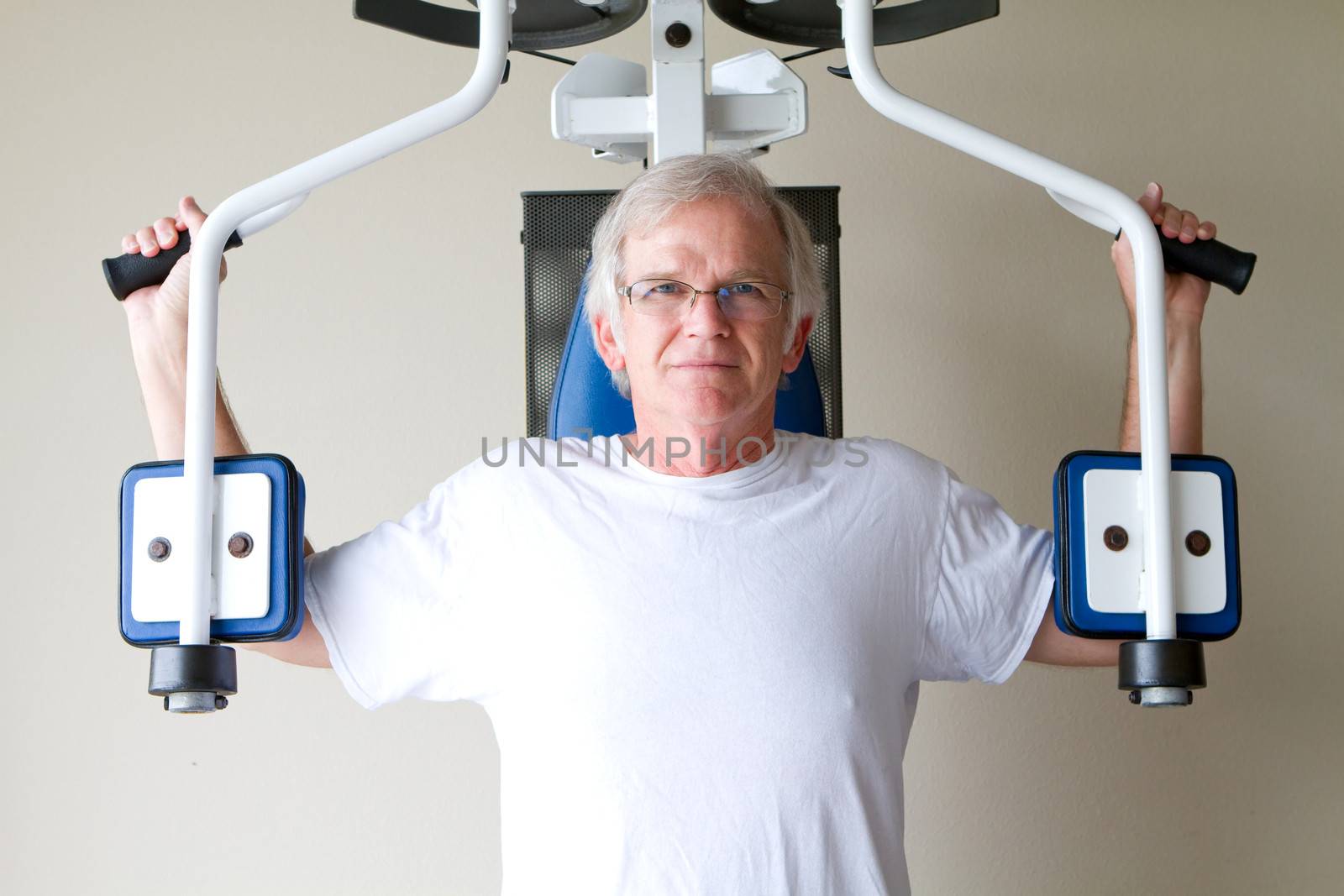 Elderly retired man uses weight training equipment at a gym to improve his health and life.