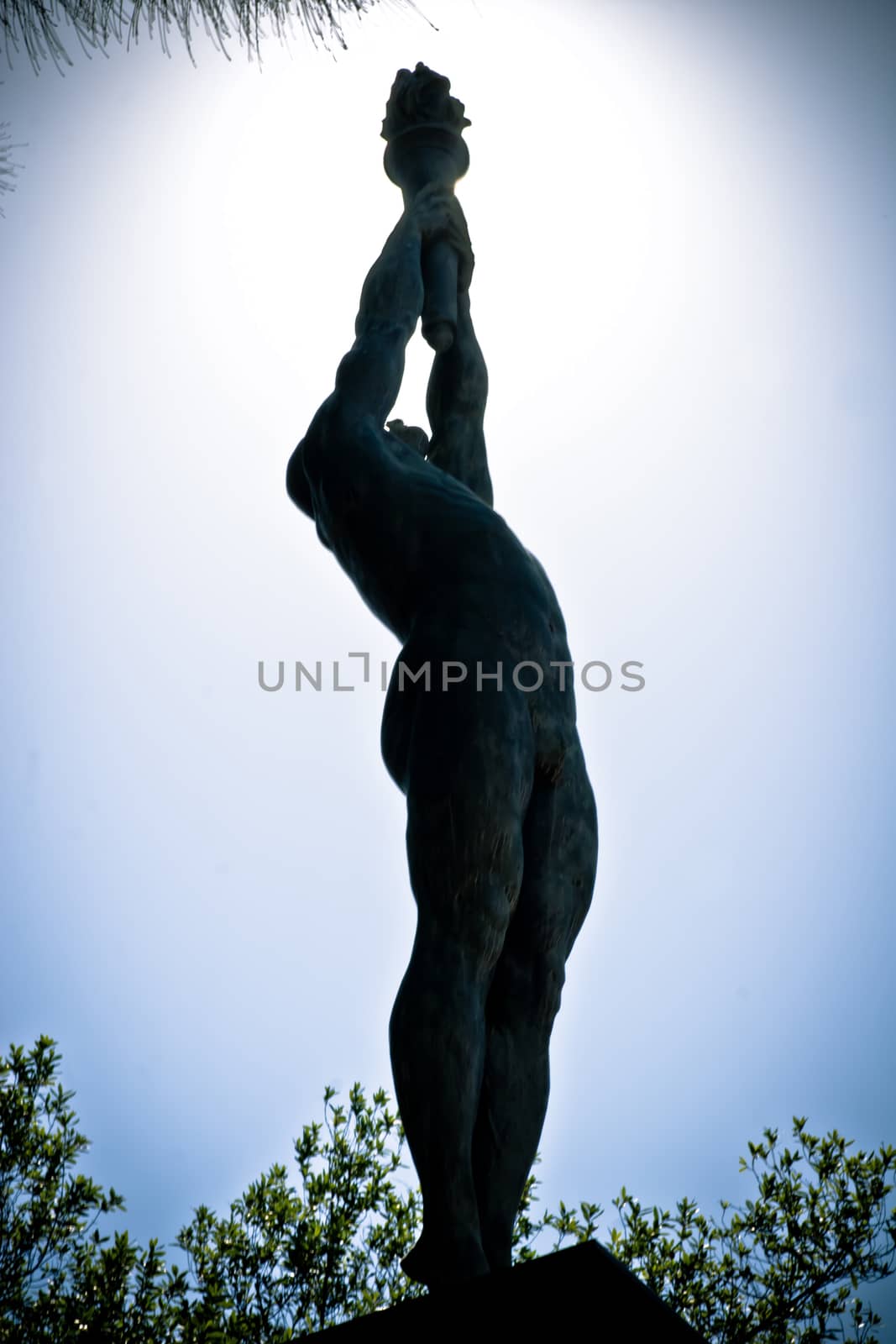 Statue of an Olympic athlete holding a torch silhoutted against a blue sky in Olympic Park, Barcelona