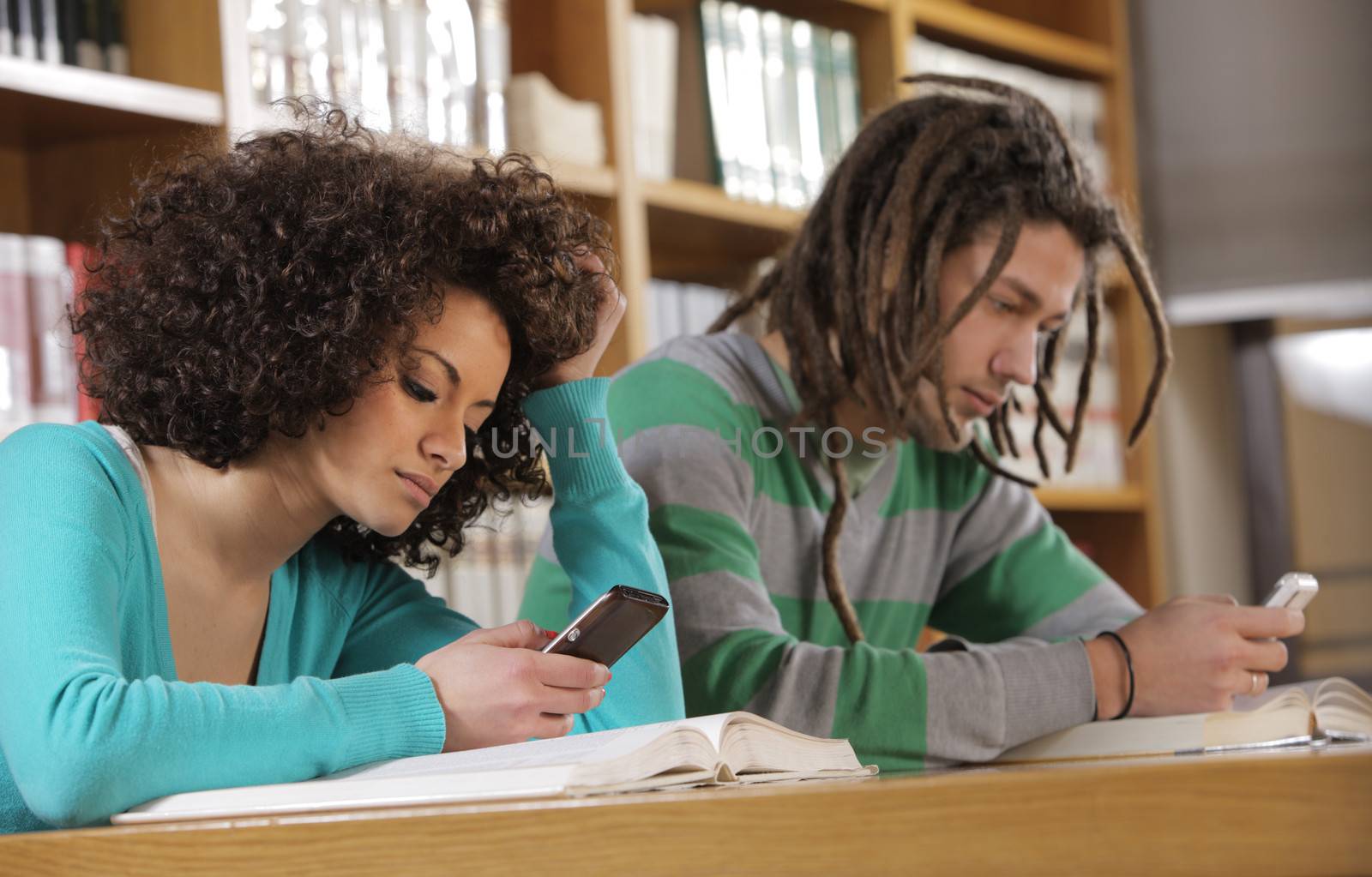 Two college students texting text messages on library