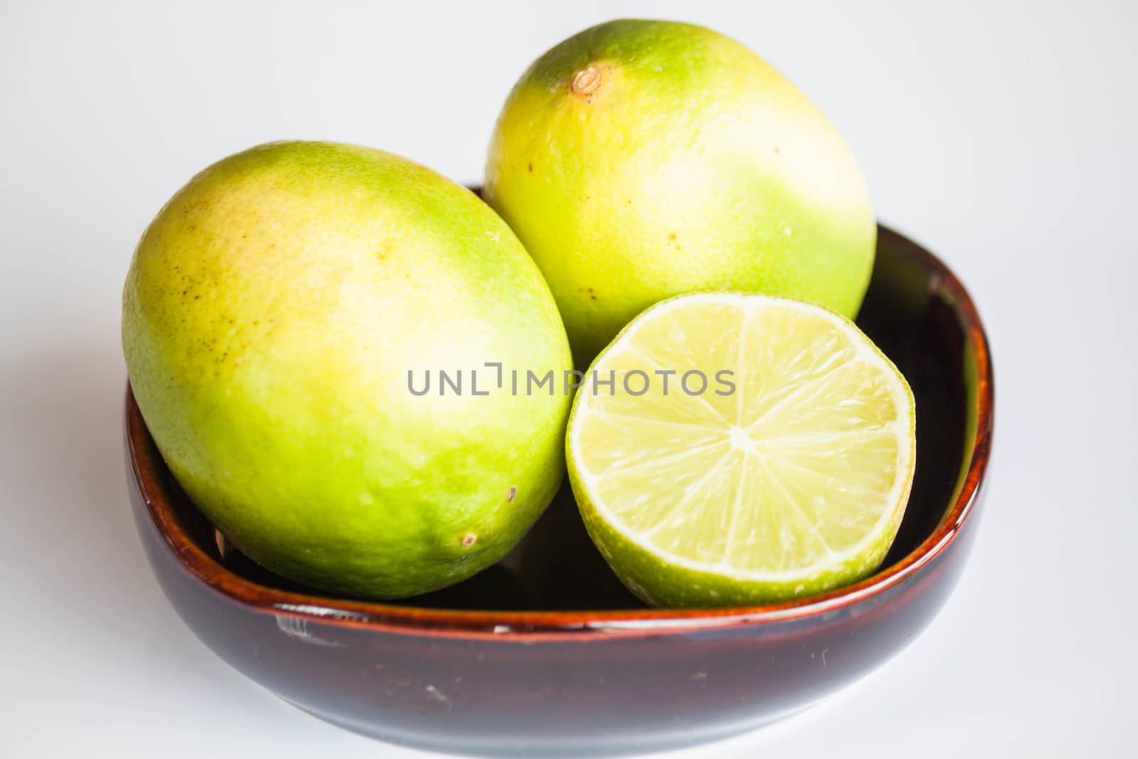 Fresh limes whole and slice in ceramic bowl  by punsayaporn