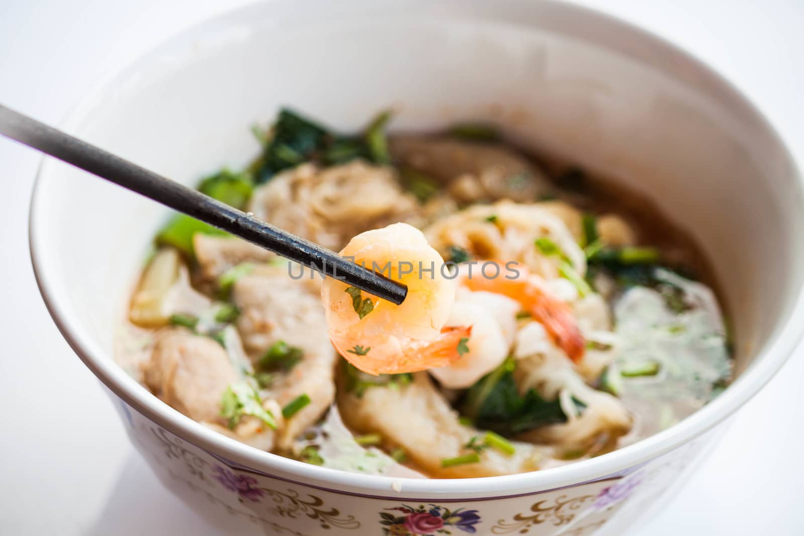 Hand hold prawn with chopsticks of thai style spicy noodles soup