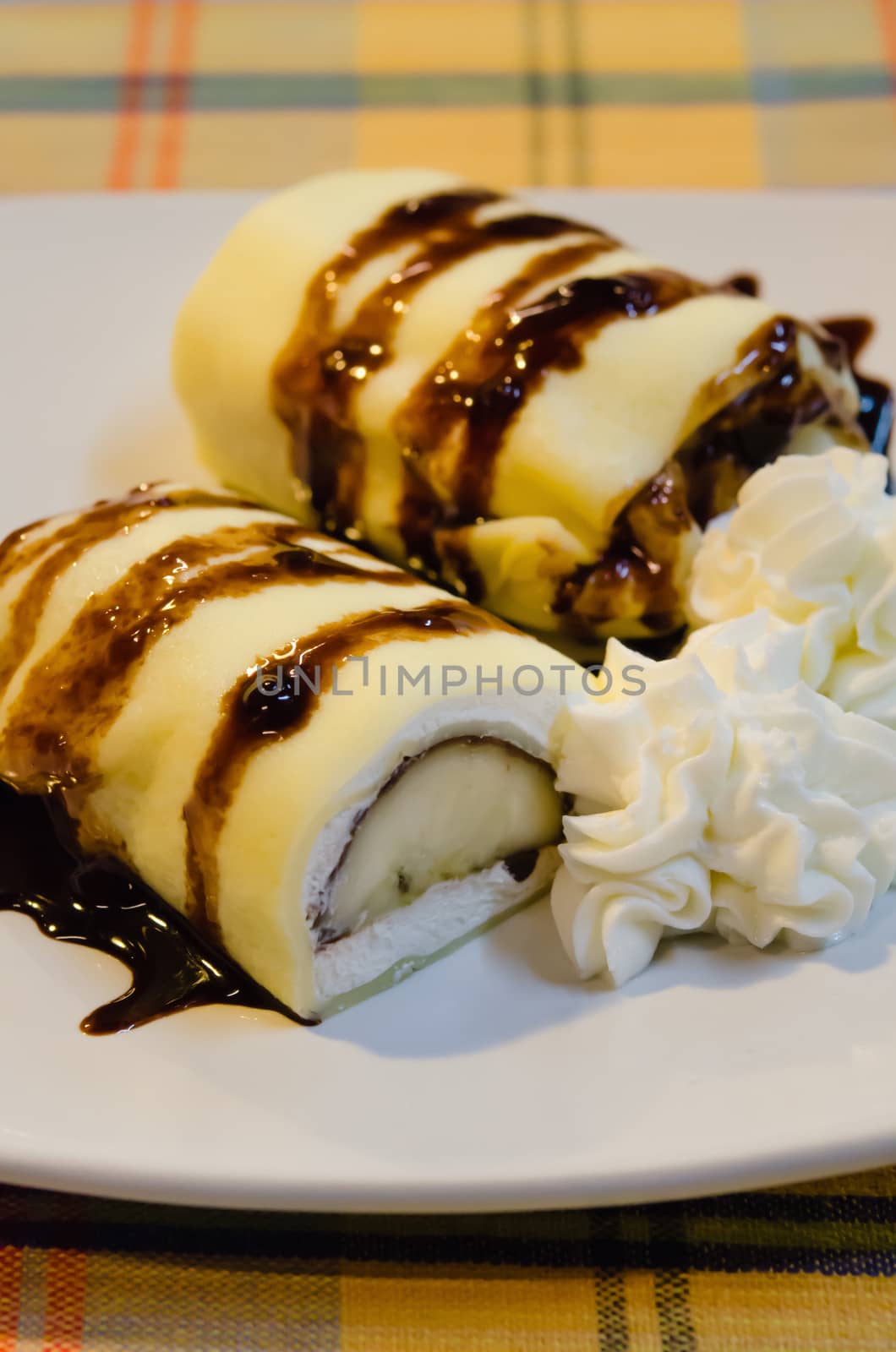banana crepe rolls filled  with white cream and banana,   topping with chocolate  syrup served with whipping cream