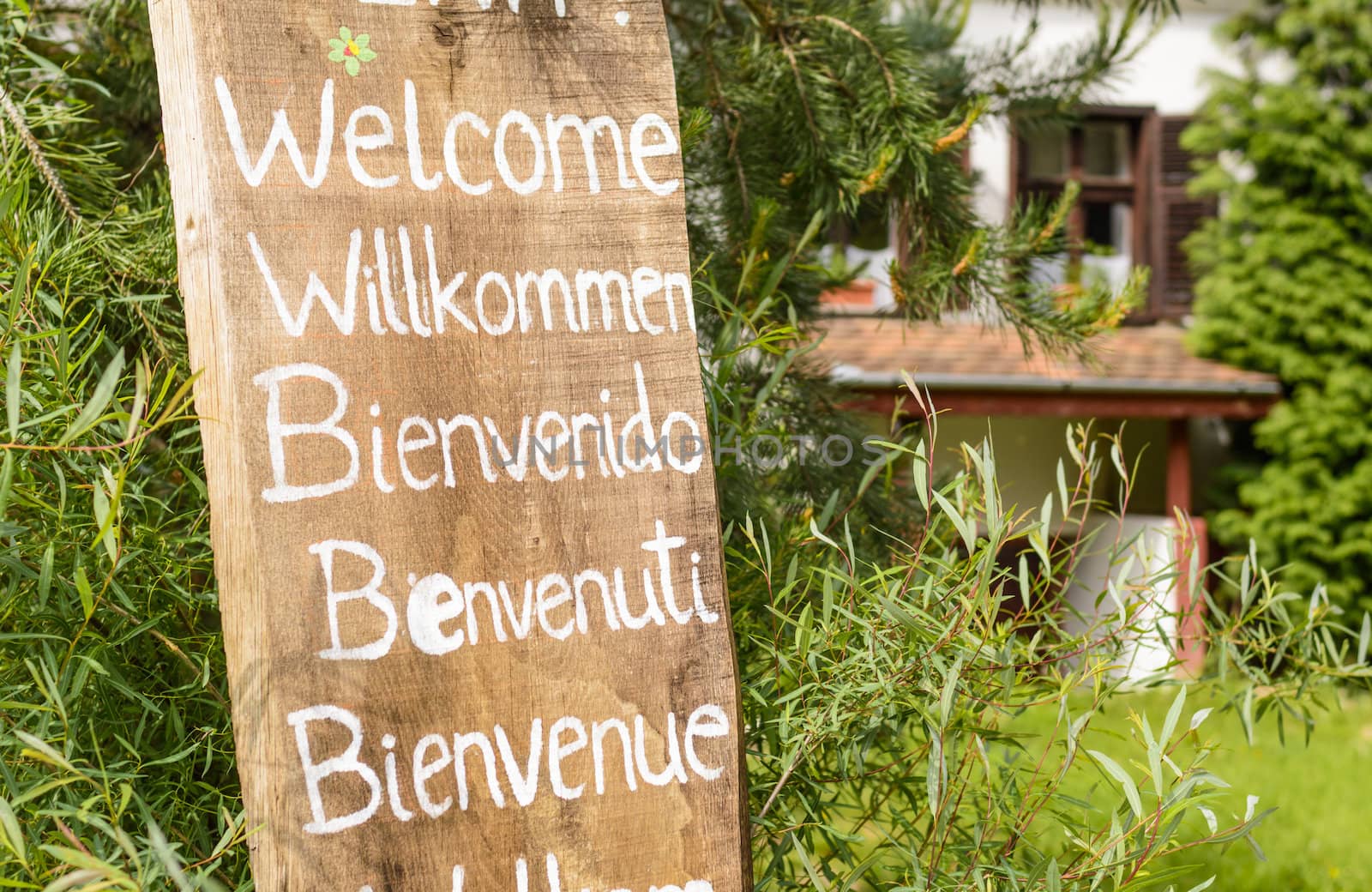 welcoming sign written with white paint on an old piece of wood in different languages