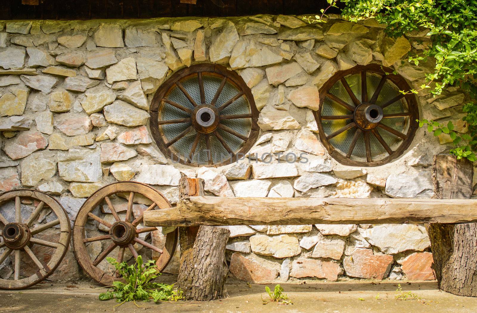 wooden bench in front of a farmhouse with stone wall and wheels wagon shaped windows