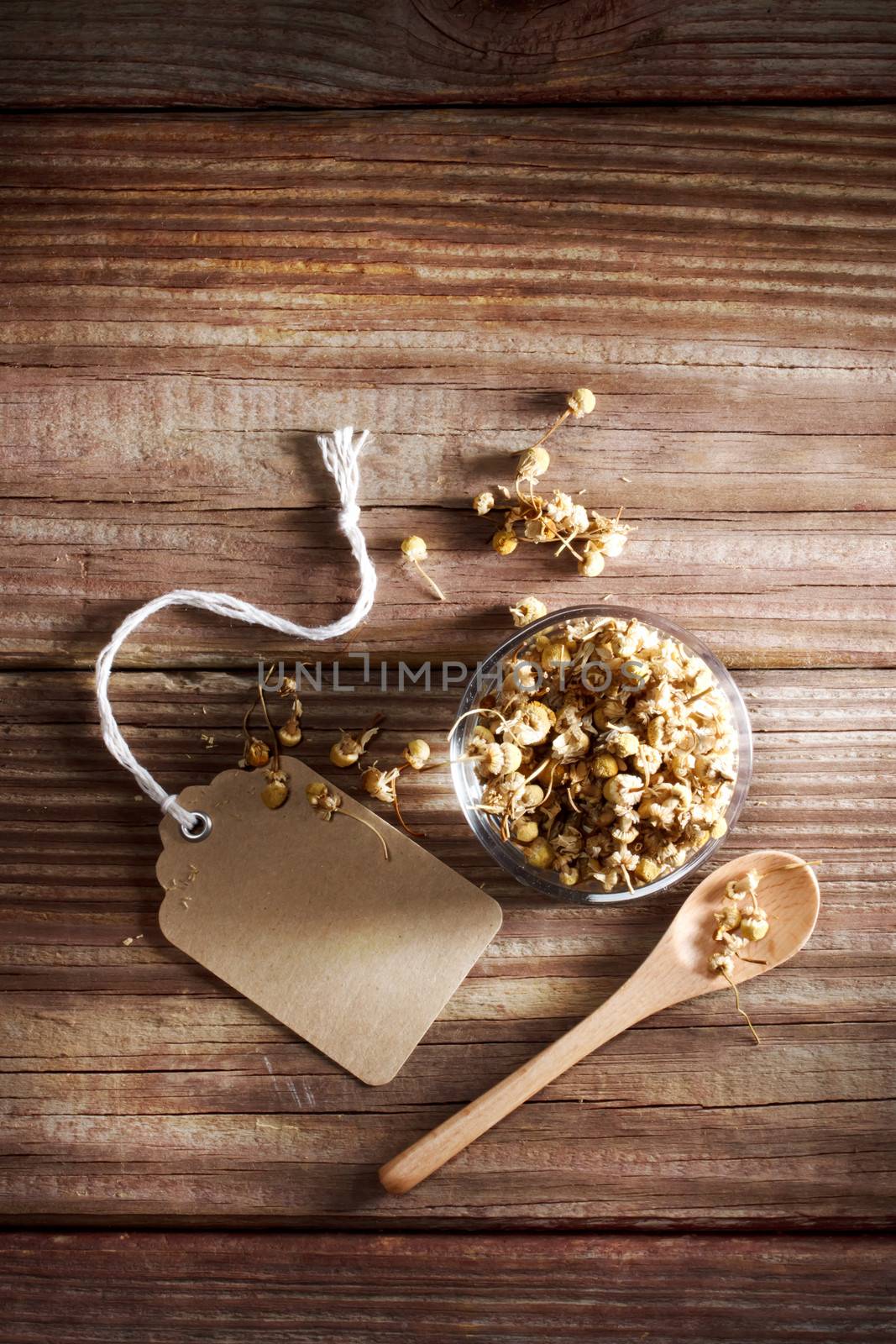 Dried Chamomile Tea in a small glass bowl on a rustic wooden table with a small spoon, and tag 