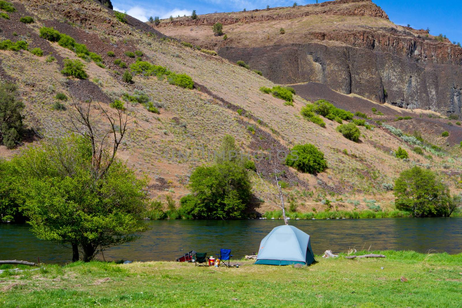 A rustic tent campsite on the Deschutes River in Oregon shows a tent setup next to a boat and the river. This is form a float camping trip.