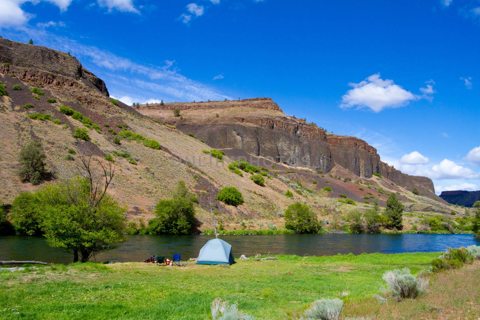 A rustic tent campsite on the Deschutes River in Oregon shows a tent setup next to a boat and the river. This is form a float camping trip.