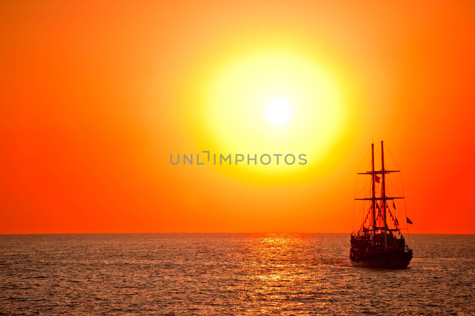 Tall ship drifting in the open sea at sunset.