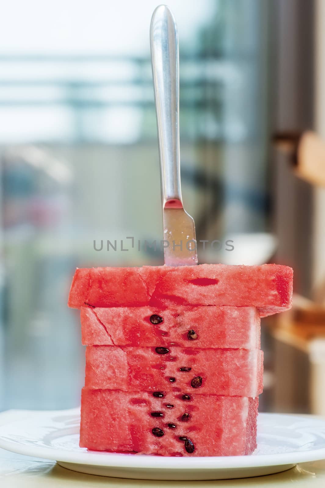 Watermelon slices are stacked on a silver platter and they stuck a table knife.