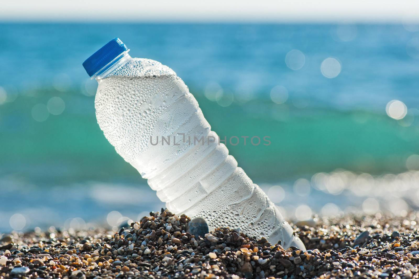 Bottle of fresh water is on the sand by the sea.