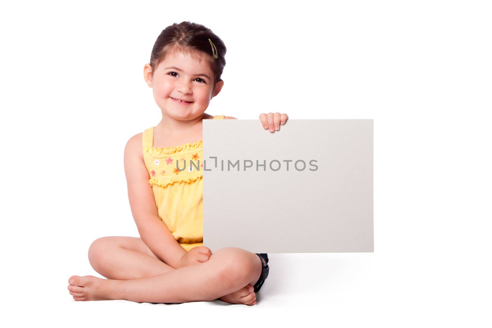 Cute happy smiling girl wearing summery yellow shirt sitting while holding whiteboard.