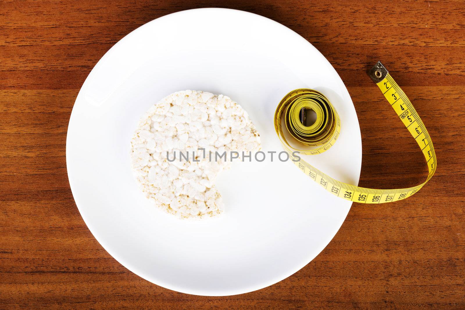 Diet concept. Biten rice cake on plate next to measuring tape.