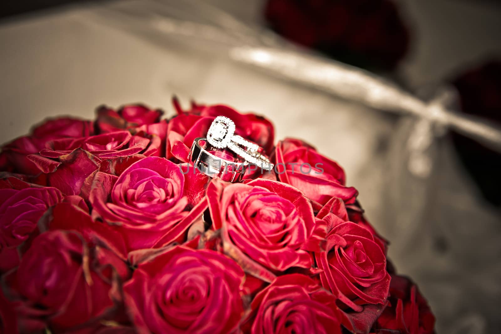 Decorative wedding rings on a posy of fresh red roses signifying love, antique look toned image
