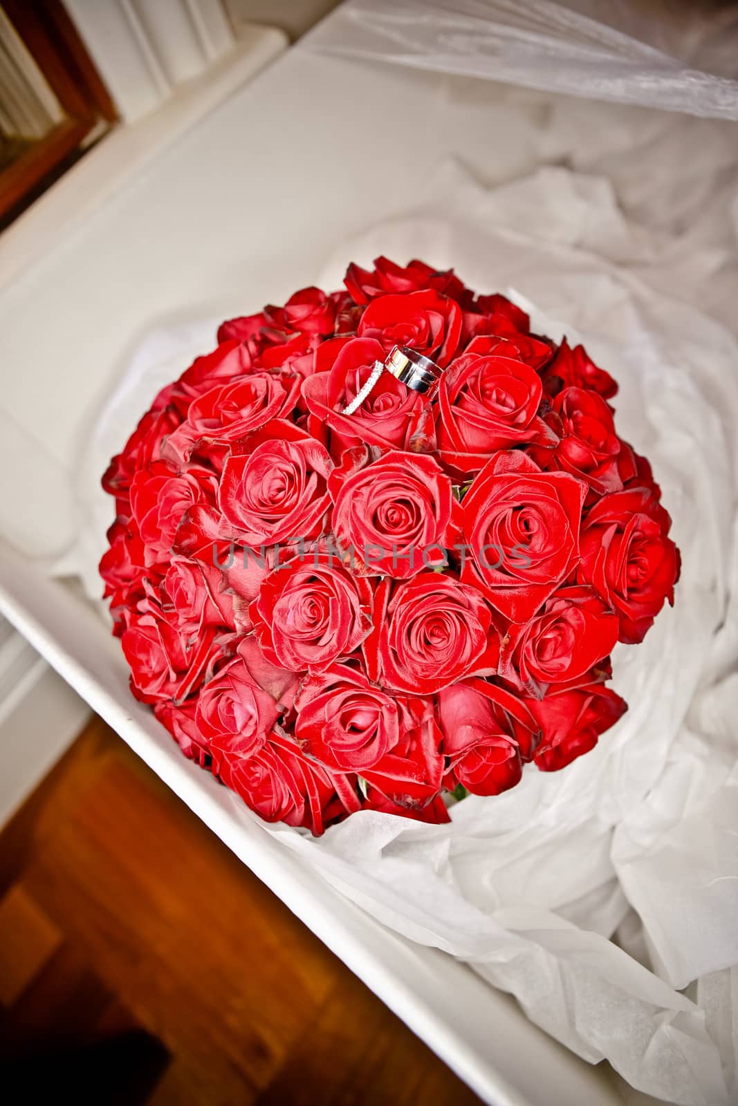 Wedding rings resting on a bridal bouquet of fresh red roses nestling in tissue paper in a box