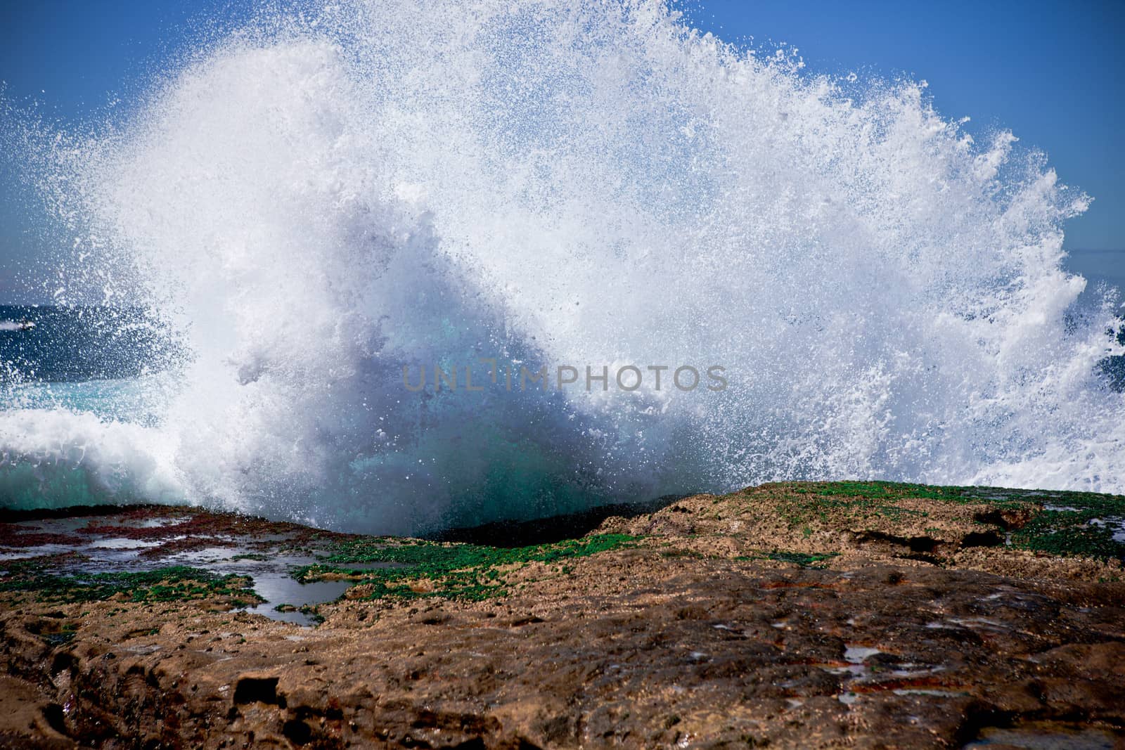Coastal breaker wave splashing rocks by jrstock