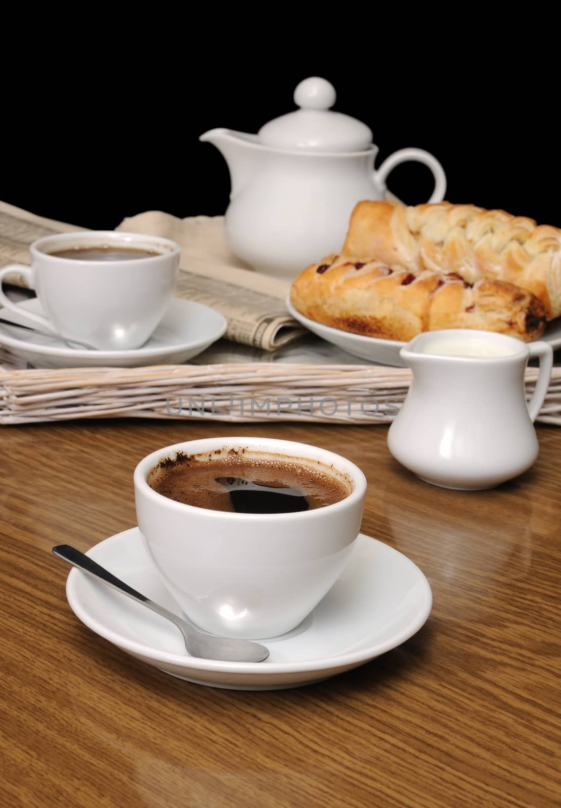 cup of fragrant black coffee on the table with newspaper and pastries