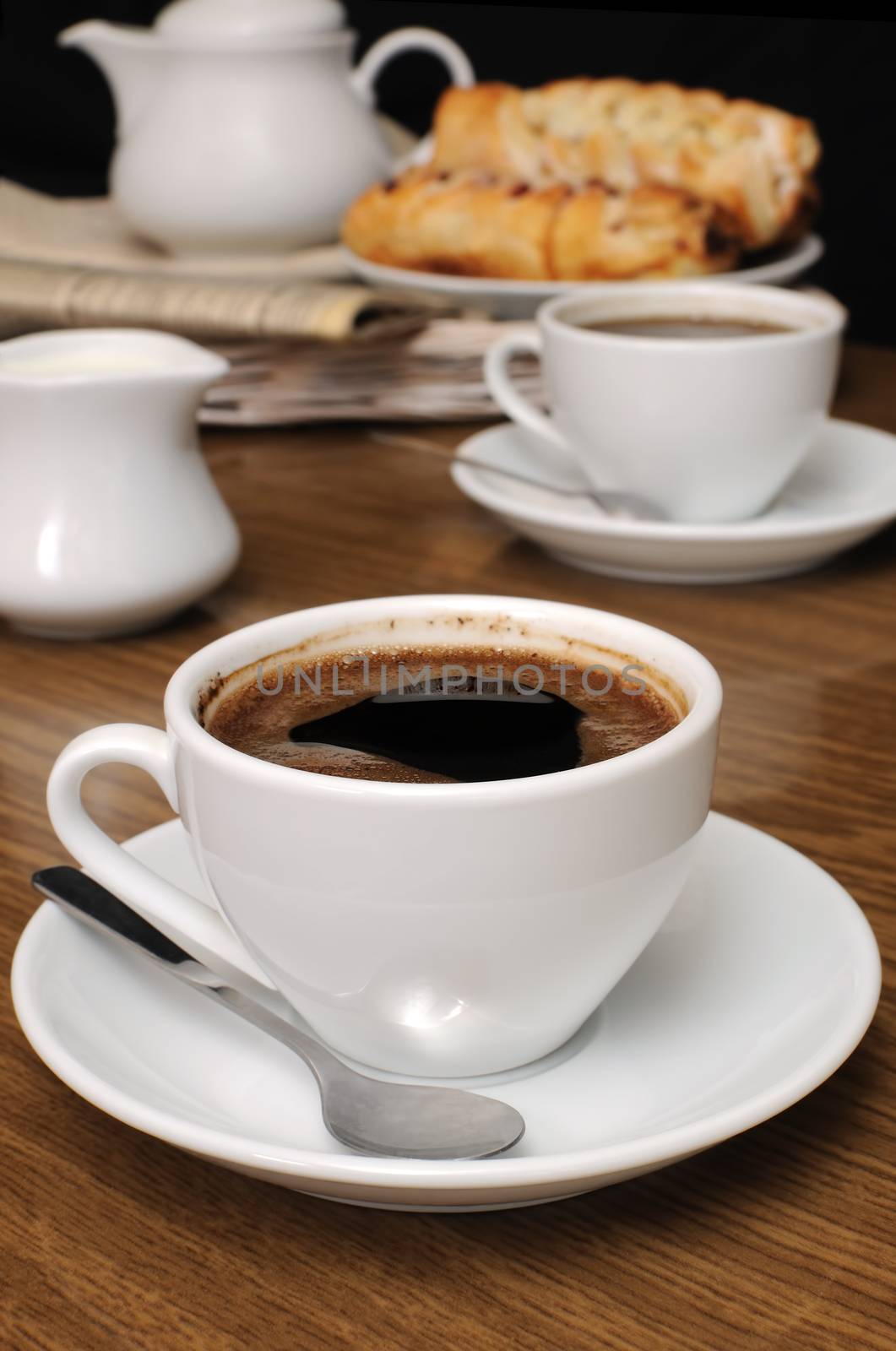  Cup of black coffee on the table with the milkman and biscuits on a tray with newspaper