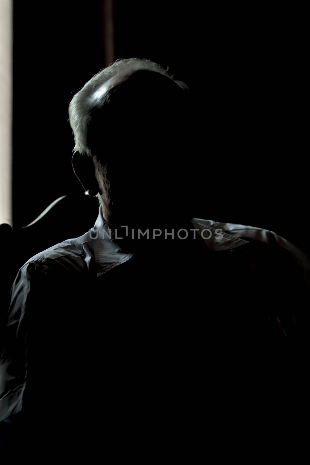 Vertical color portrait silhouette of a seated male man gentleman back lit from a doorway of an old building in a commercial services posture. Shot location was the Ashram at Pondicherry, Tamil Nadu India