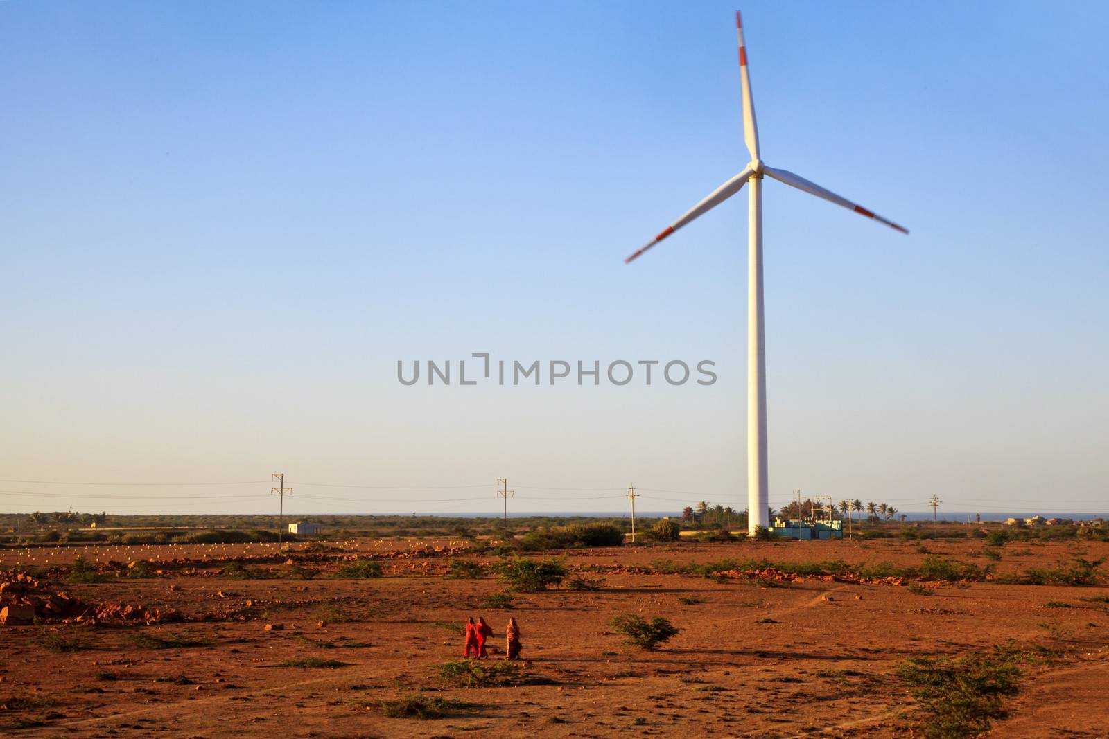 Horizontal color landscape captured in Gujarat India in the early morning before the sun rises of a group of women walking away across barren fields and a windmill generator