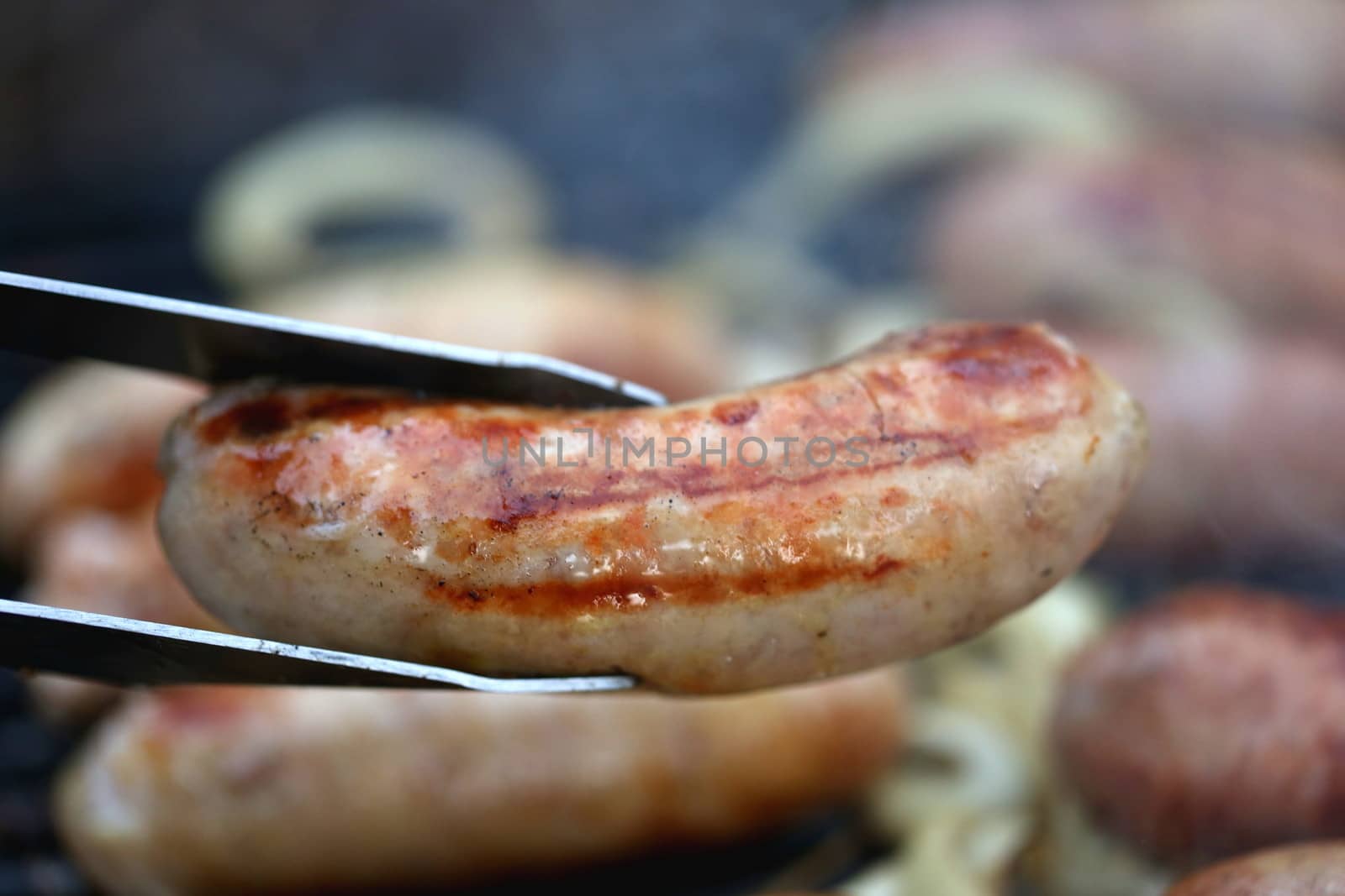 A pork sausage barbecued and barbecue tongs by indigolotos