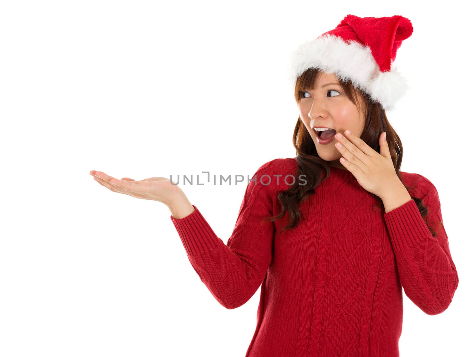 Christmas girl showing empty palm with copy space smile surprisingly standing isolated on white background. Beautiful young smiling woman in red Santa hat showing copyspace. Asian Chinese / Japanese female model.