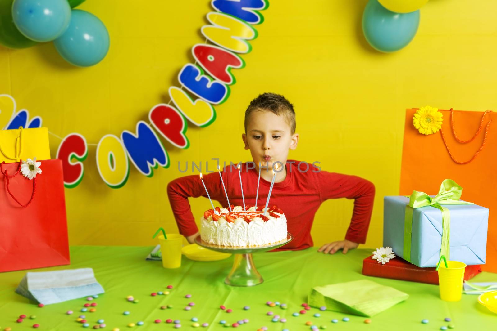 Child during his birthday party blowing out candles on her beautiful and good strawberry cake.