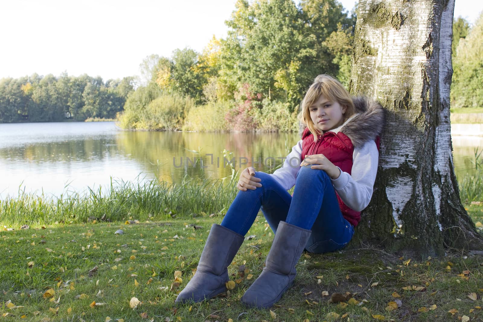 a little girl sitting under tree in autumn park by the lake