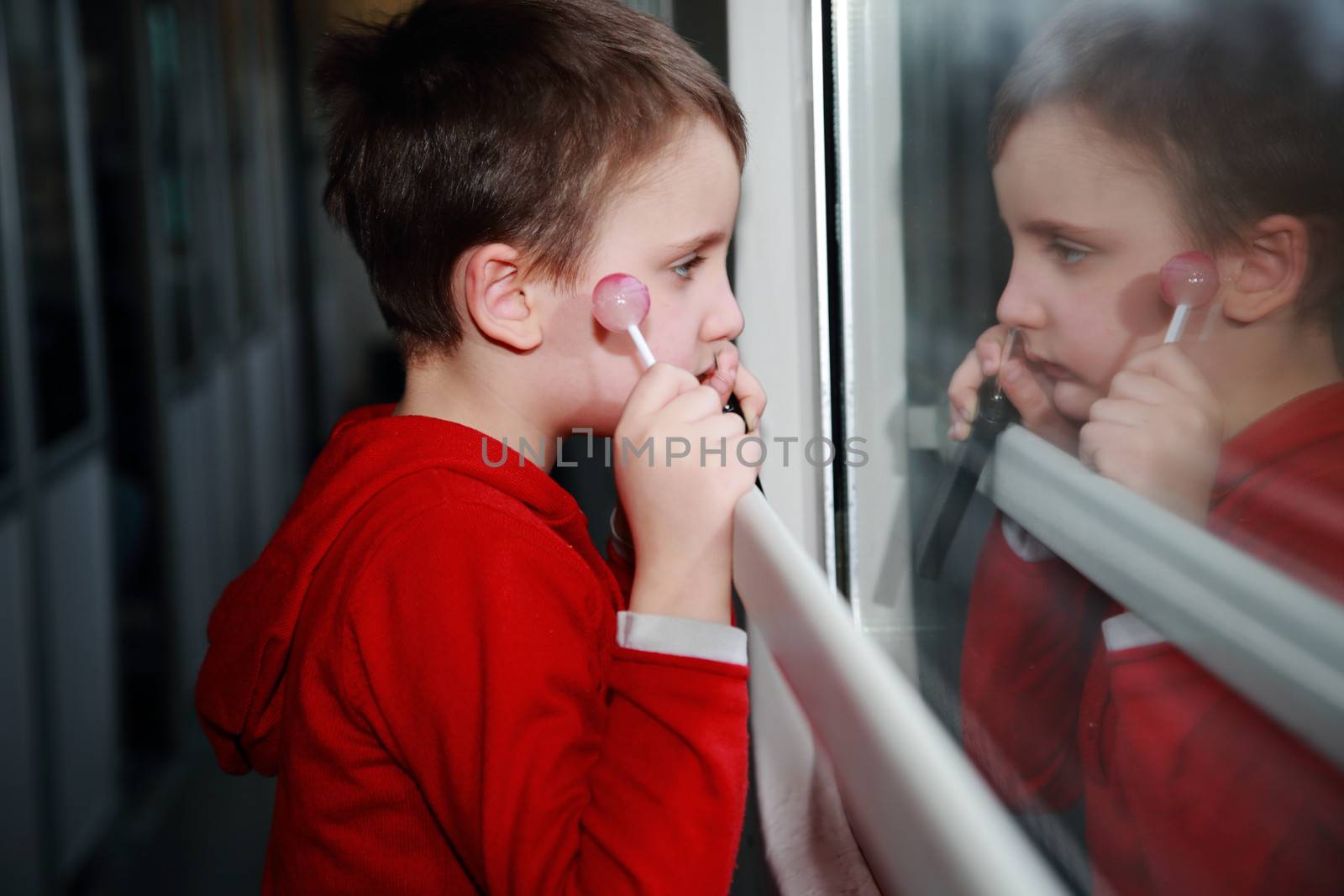 During a trip on a train a child with dreamy eyes looking out the window while eating a lollipop.