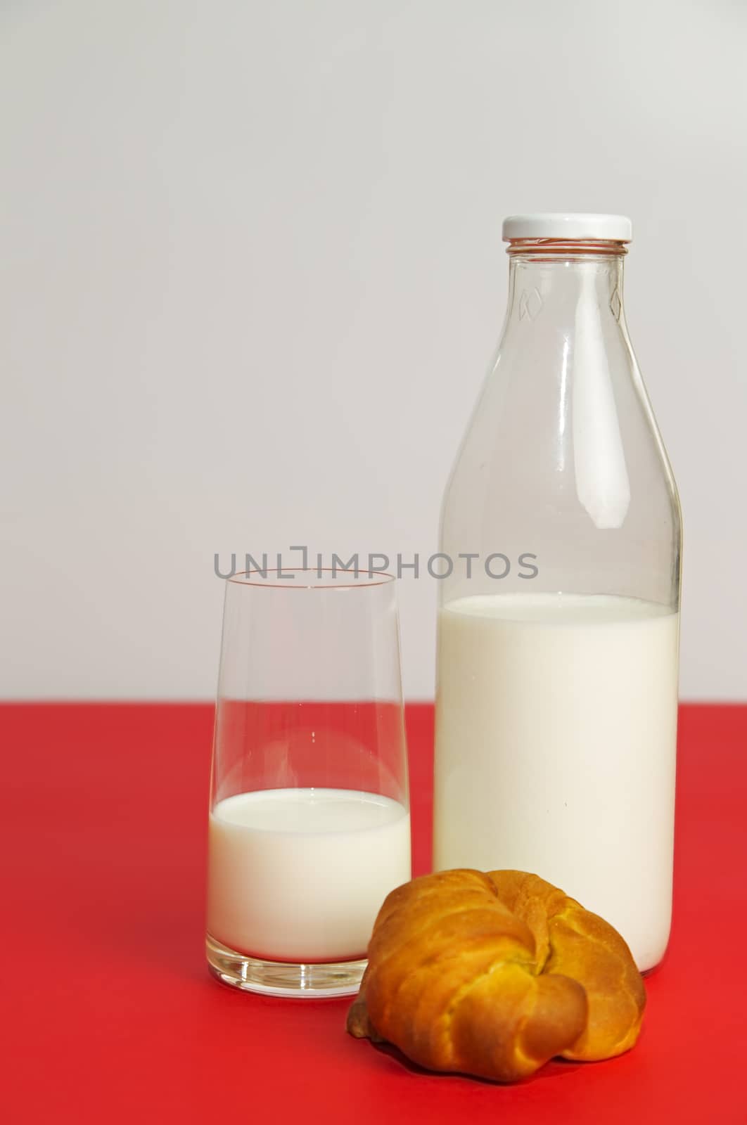 In the kitchen, on the red table, glass with fresh milk and croissants on a white background.