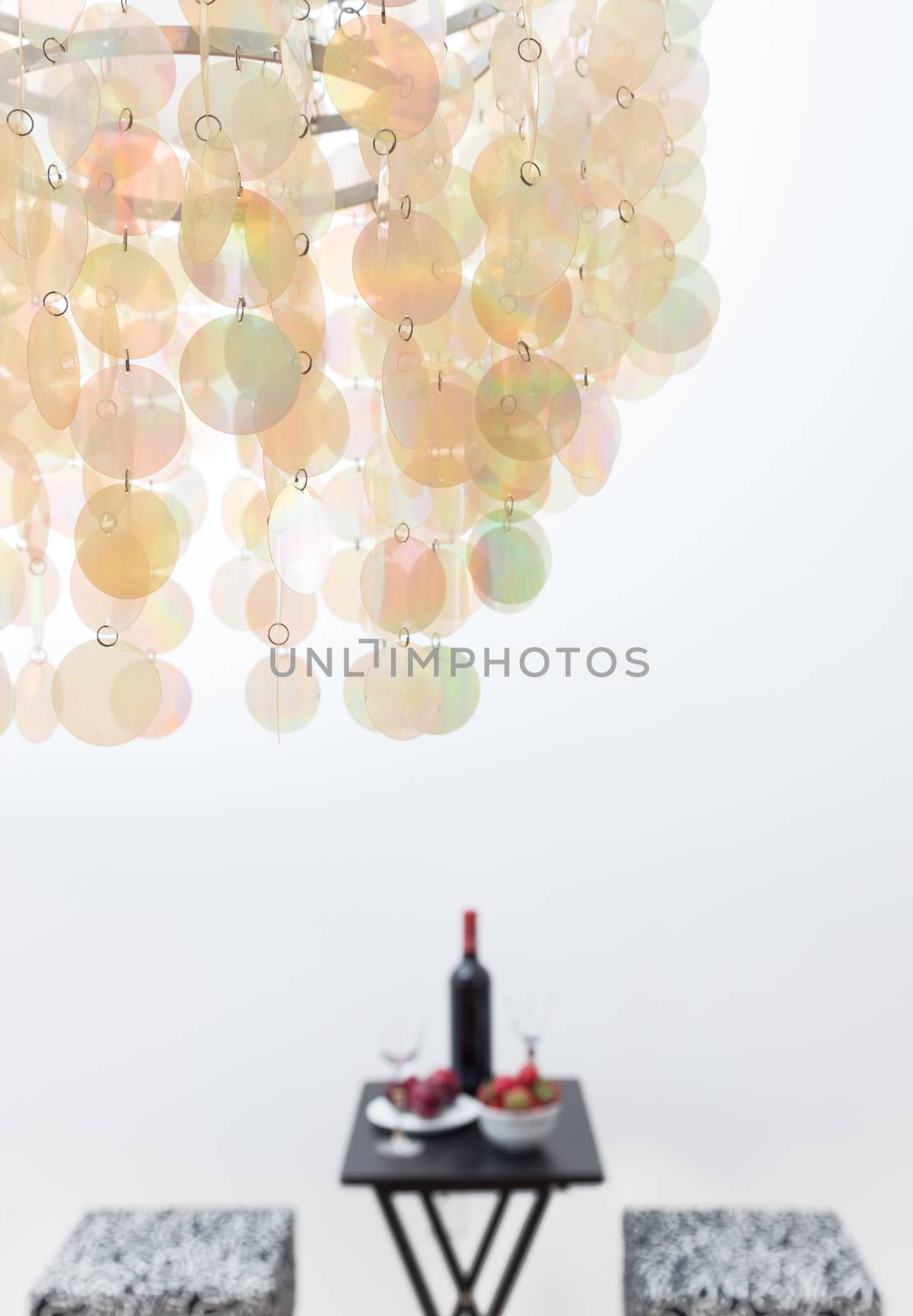Bottle of red wine on a table, in a room decorated with beautiful chandelier. Focus on chandelier.