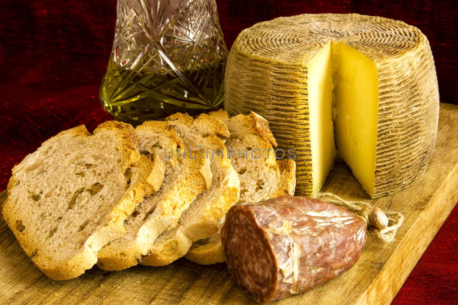 Mediterranean food: sheep cheese, salami, bread with walnuts and olive oil on a wooden cutting board on a dark red background.