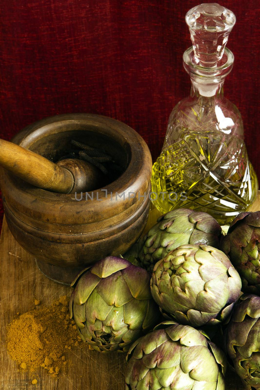Mediterranean food: artichokes and spices such as curry and long black pepper in a mortar and pestle and olive oil bottle on dark red background.