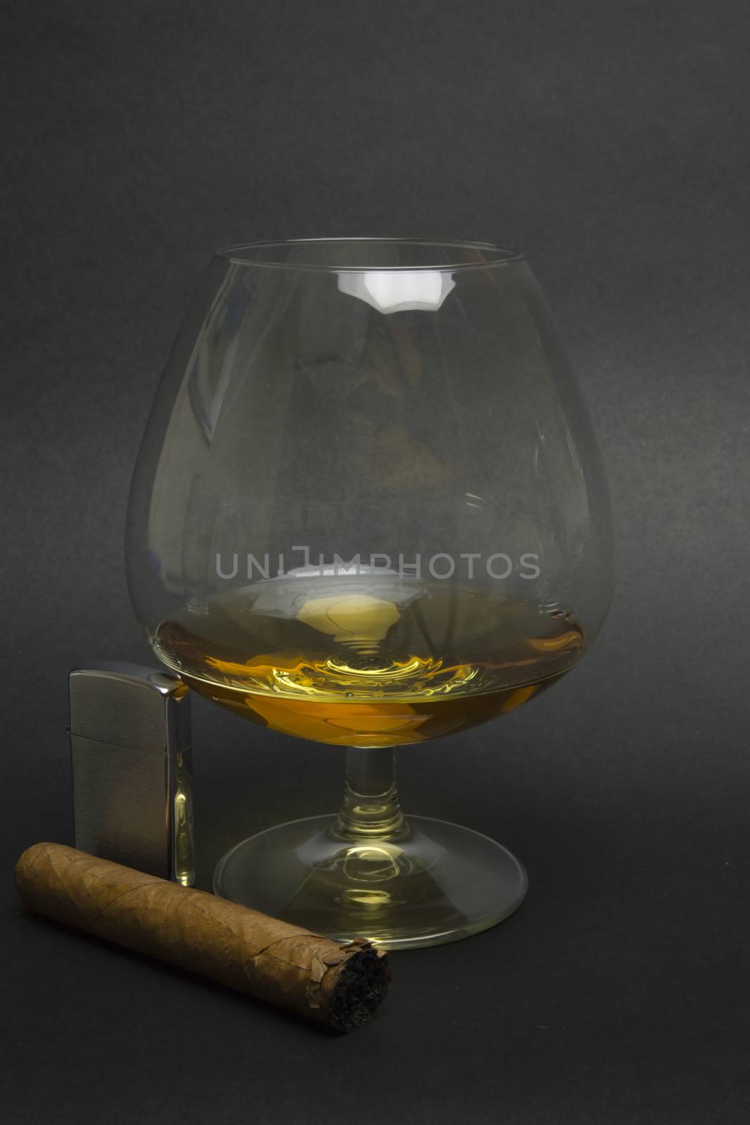 Balloon of cognac with cuban cigar and lighter beside isolated on dark background.