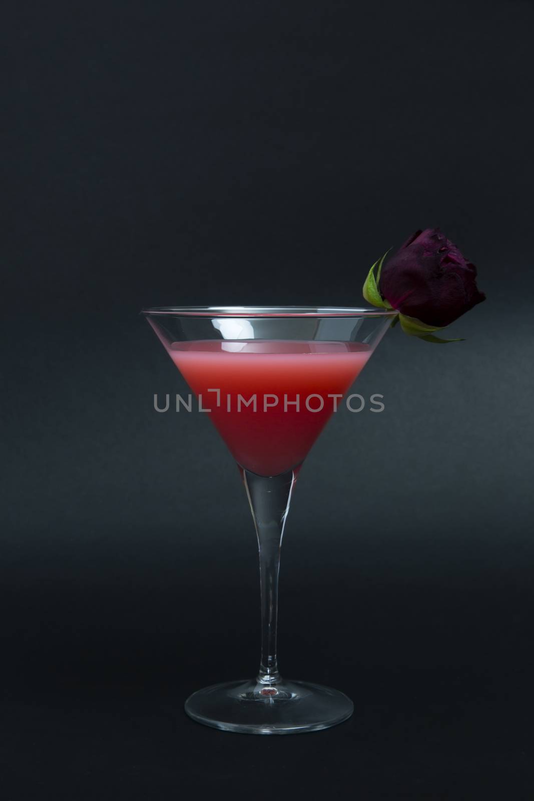 Pink cocktail made with vodka, yogurt liquor and rose syrup decorated with rosebud on dark background.
