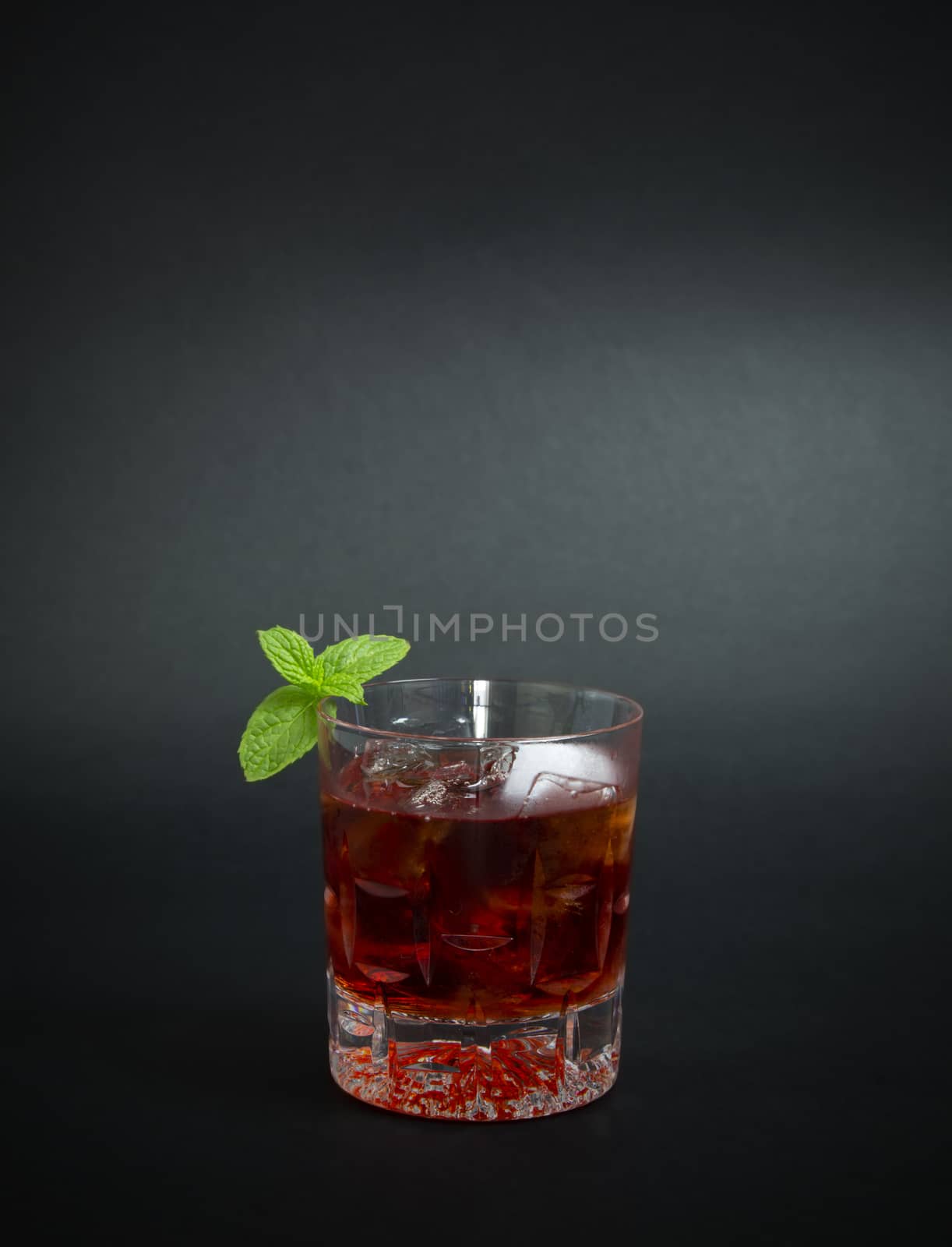 Red cocktail made with gin and red liqueur, decorated with mint twig, isolated on dark background.