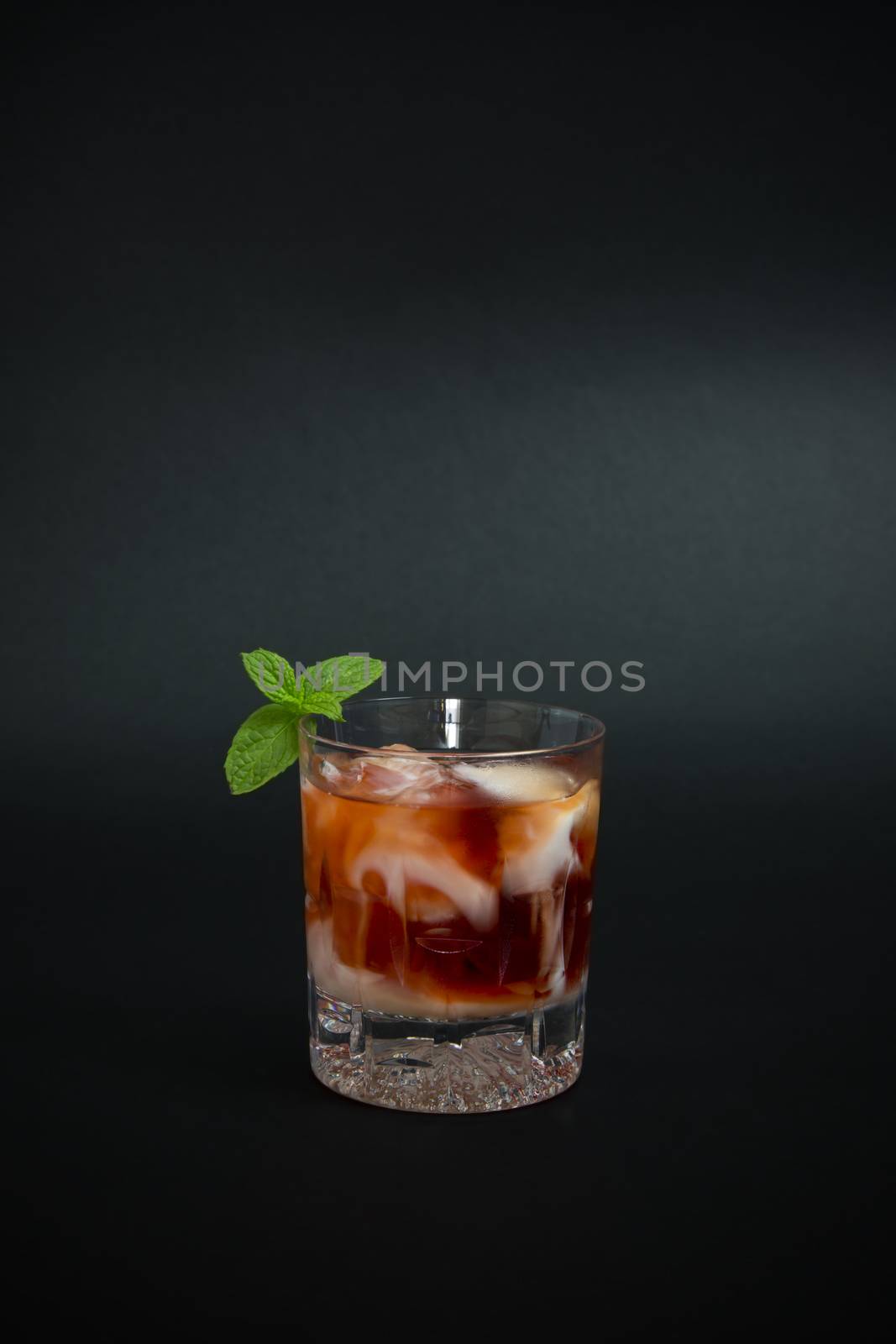 Cocktail made with vodka, red liquor and few drop of yogurt liquor on top, decorated with mint twig, isolated on dark background.