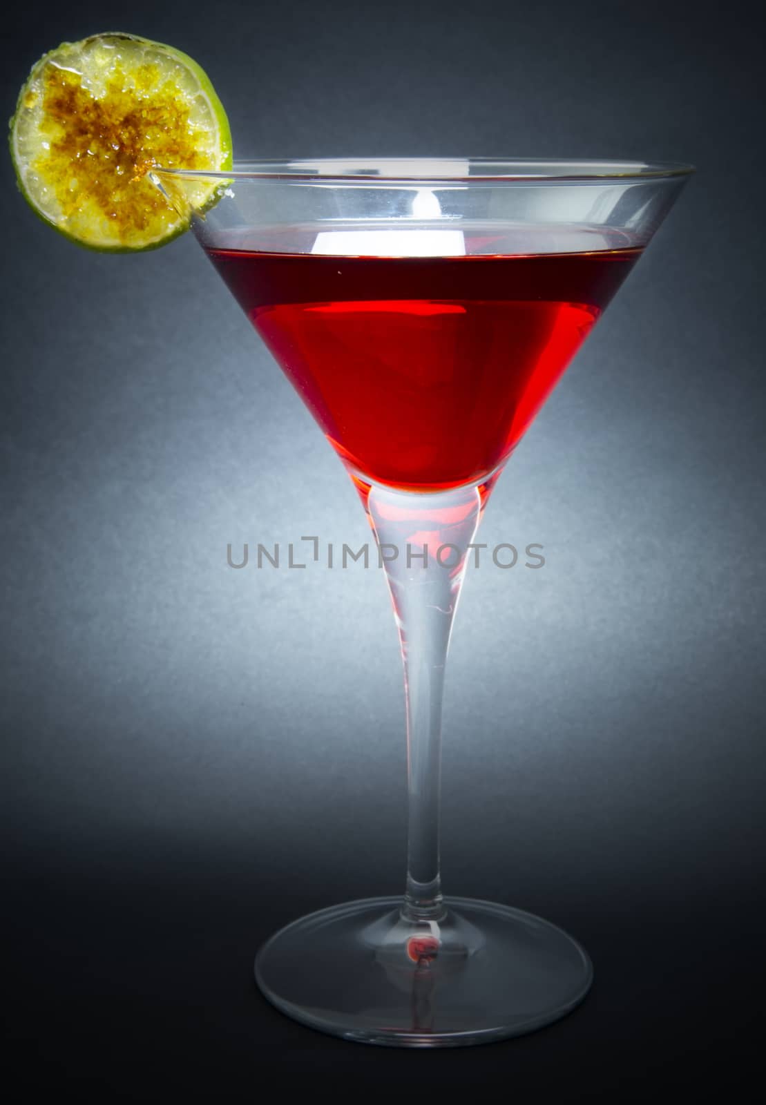 Red cocktail made with vodka and liqueur red, decorated with washer caramelized lime on dark background.