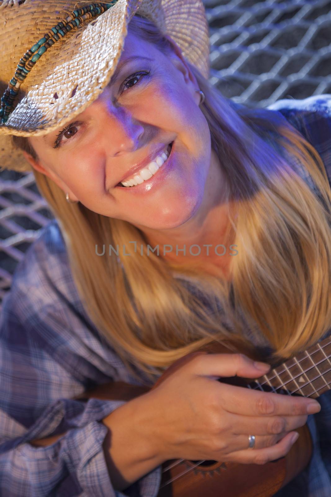 Beautiful Evening Portrait of Cowgirl Near Campfire Playing Her Ukulele.