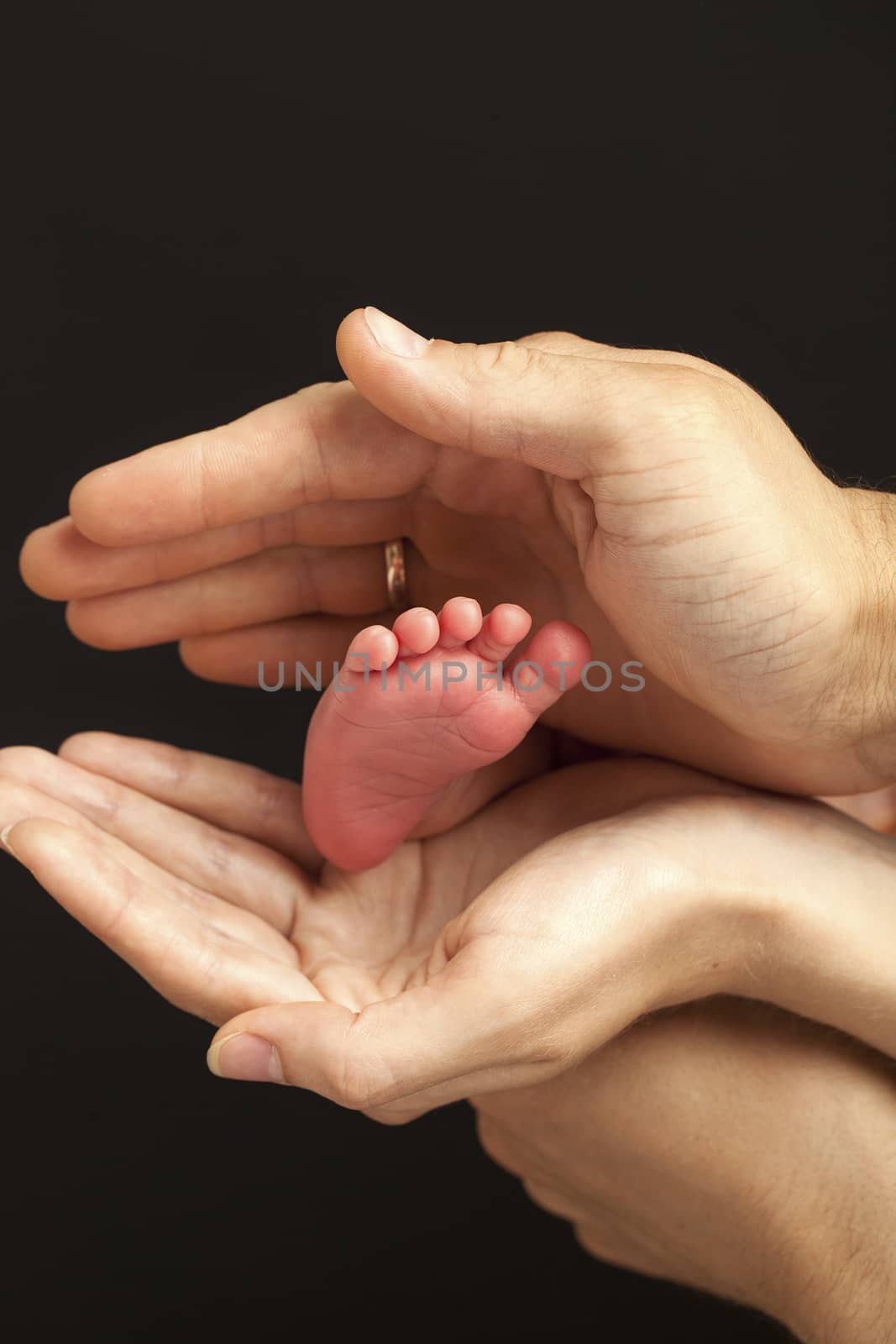 Newborn baby foot in parents hands over black background