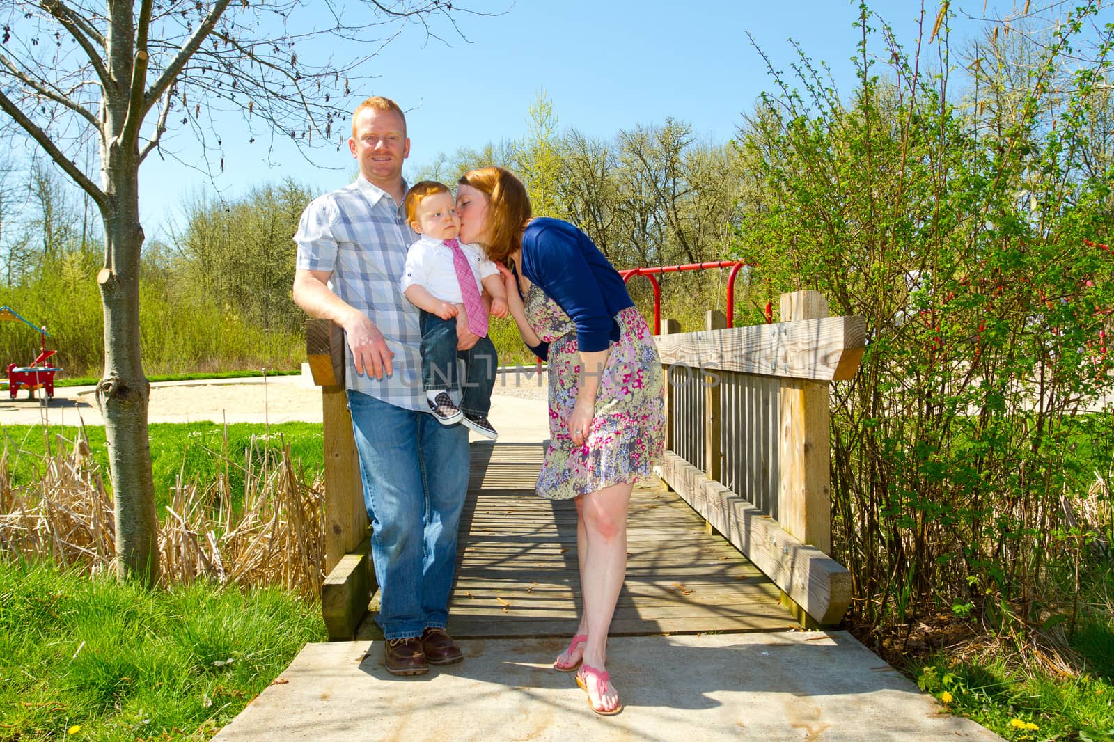 A man and a woman hold their baby one year old son while posing for a family photo outdoors.