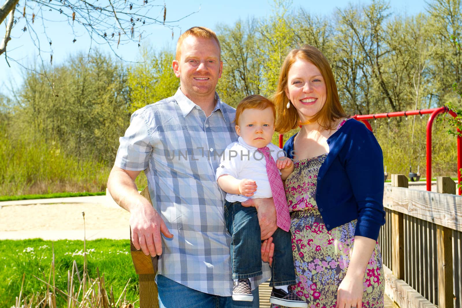 A man and a woman hold their baby one year old son while posing for a family photo outdoors.