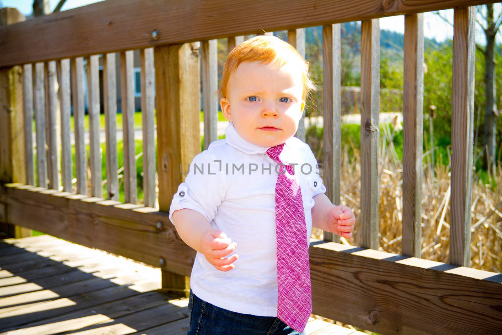 A one year old baby boy walks across a bridge wearing nice clothes and a necktie.