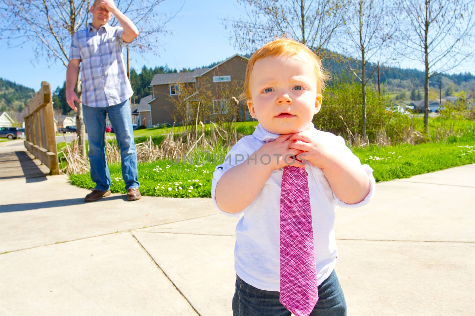 A father is holding his hand to his head in the background of this image while the young boy has his hands to his necktie.