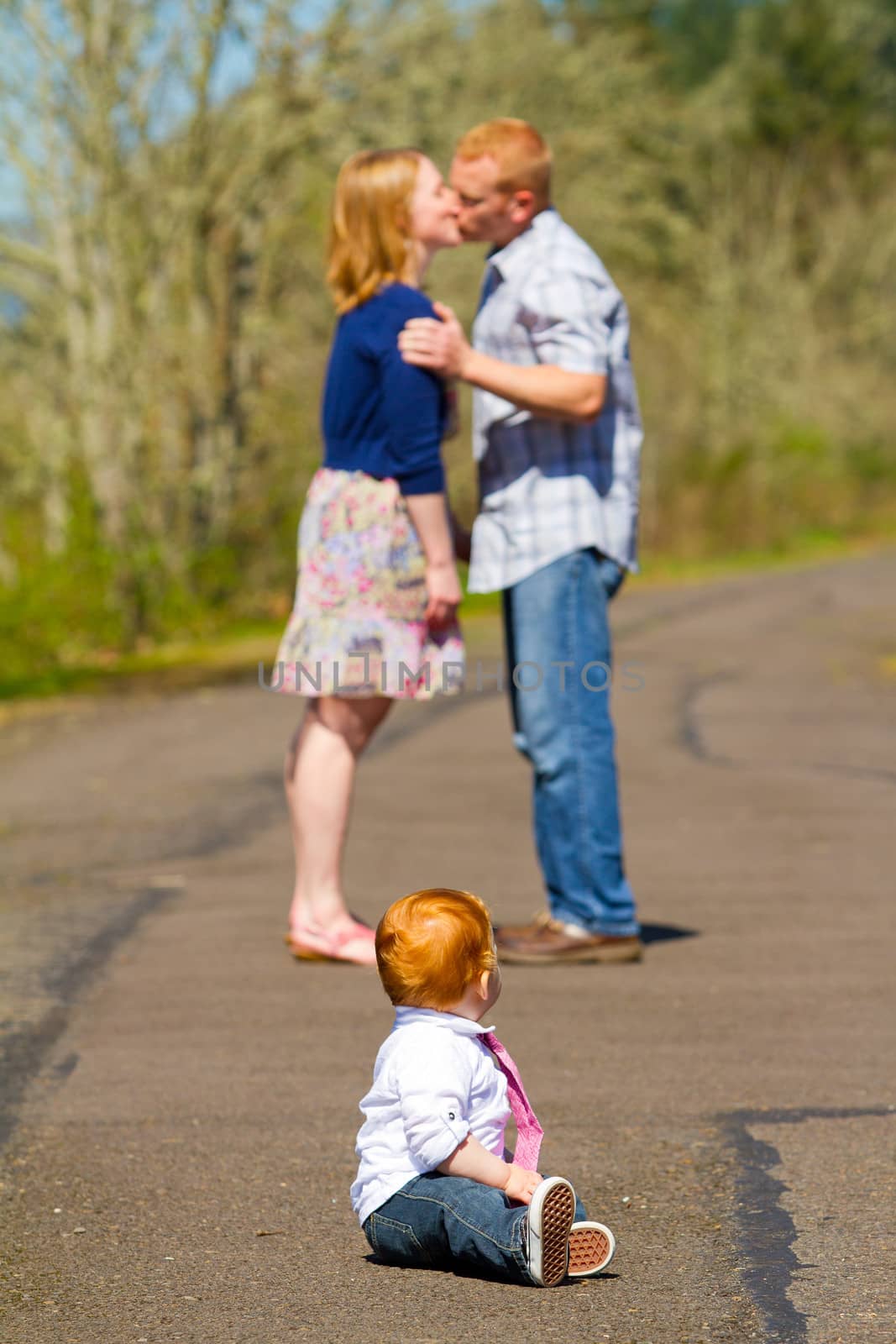 In this selective focus image the parents of a baby one year old boy are kissing out of focus in the background.